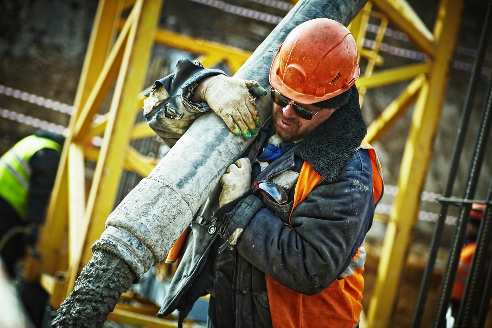 construction worker in an orange safety helmet and jacket lifts a concrete hose