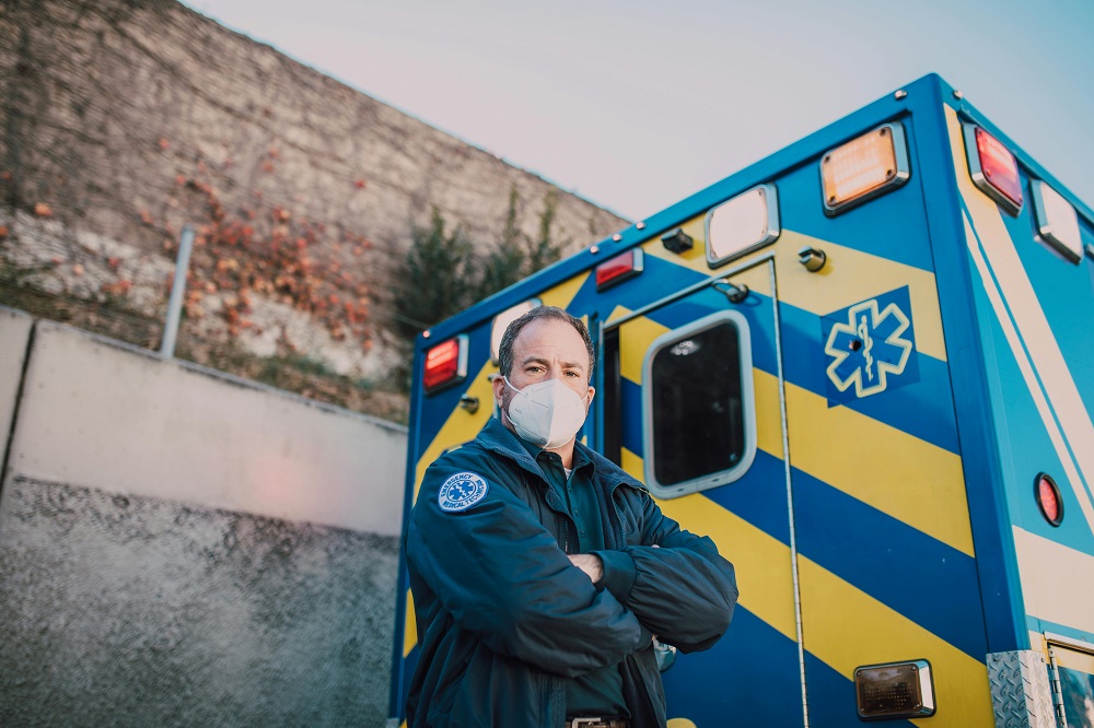 emergency responder stands beside a blue and yellow ambulance