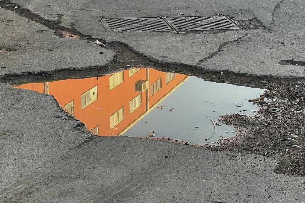 Reflection of Orange Building in Puddle on Urban Street