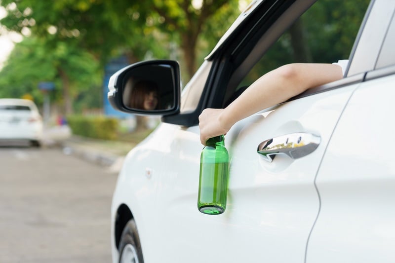 Drunk woman driving and holding beer bottle outside a car